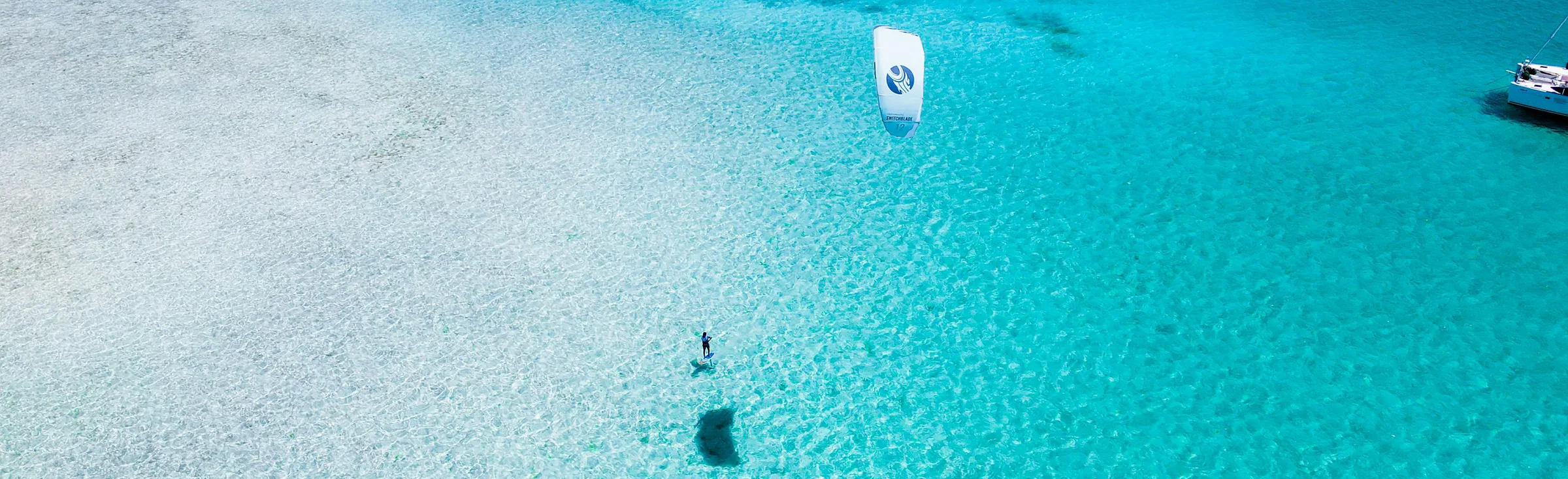 Kitesurfer alone in a turquoise lagoon with a yacht at anchor, aerial view