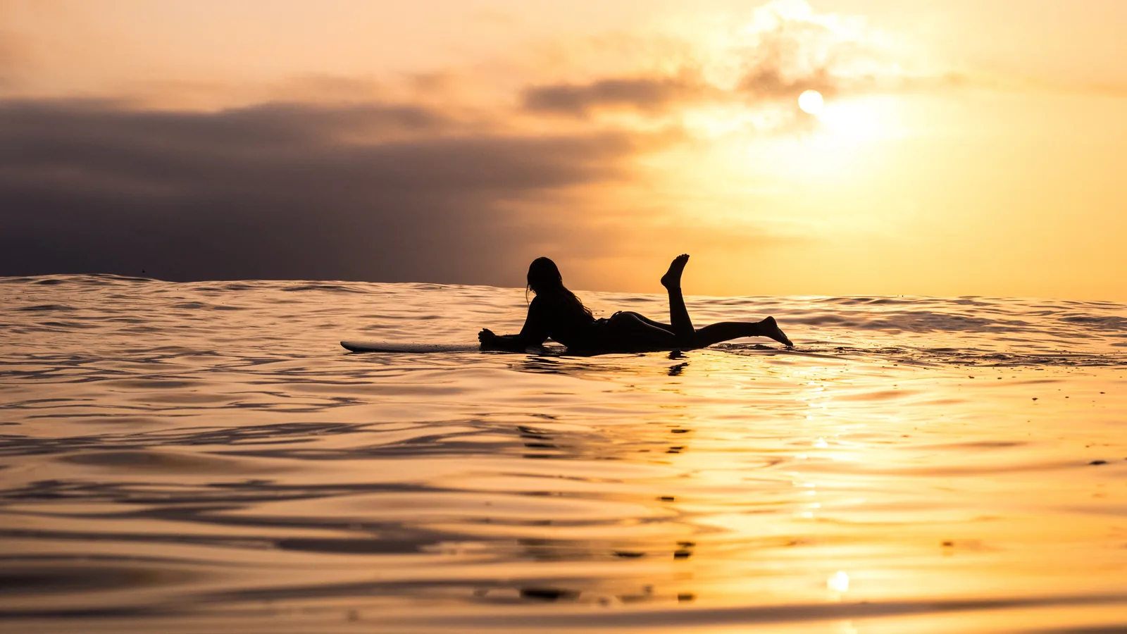 Surfer paddling on calm water at golden sunset