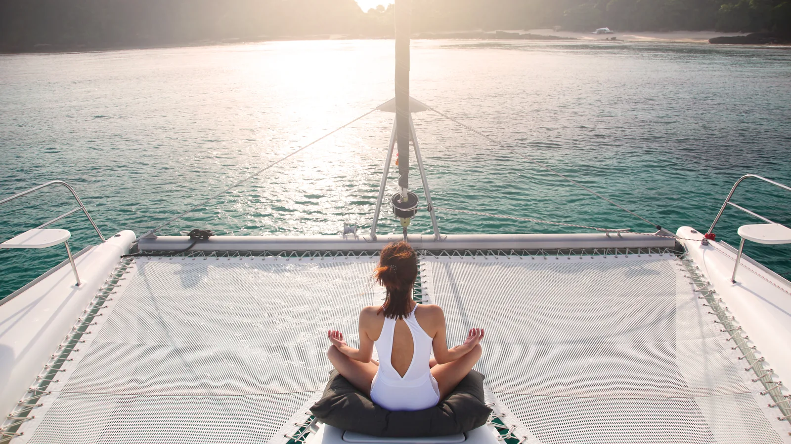 Guest meditating on the foredeck trampoline of a catamaran at anchor