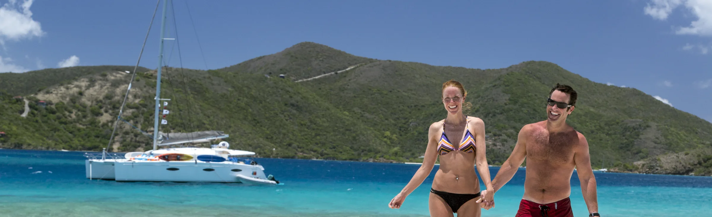 Charter guests in the British Virgin Islands, couple on the beach with their yacht in the background